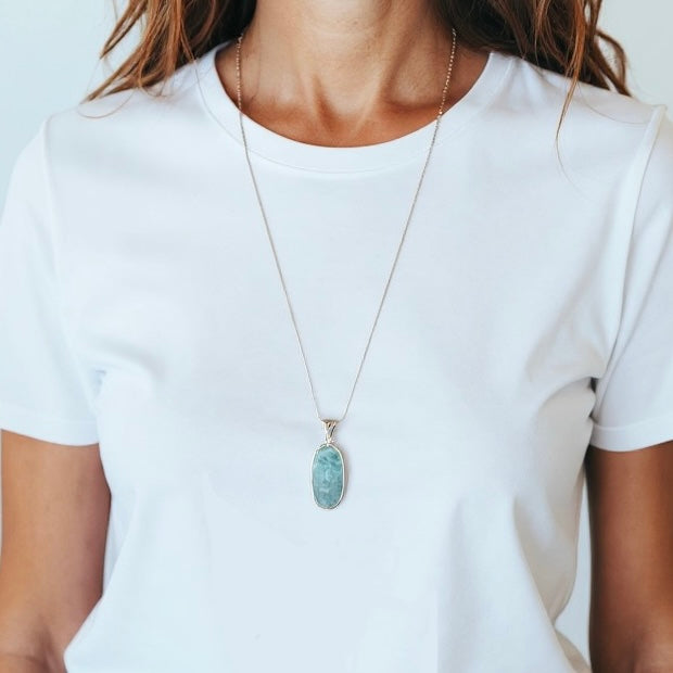 Eine Frau trägt Larimar Silber Anhänger mit einer Silber-Kette. Trägt auch ein weises T-Shirt
