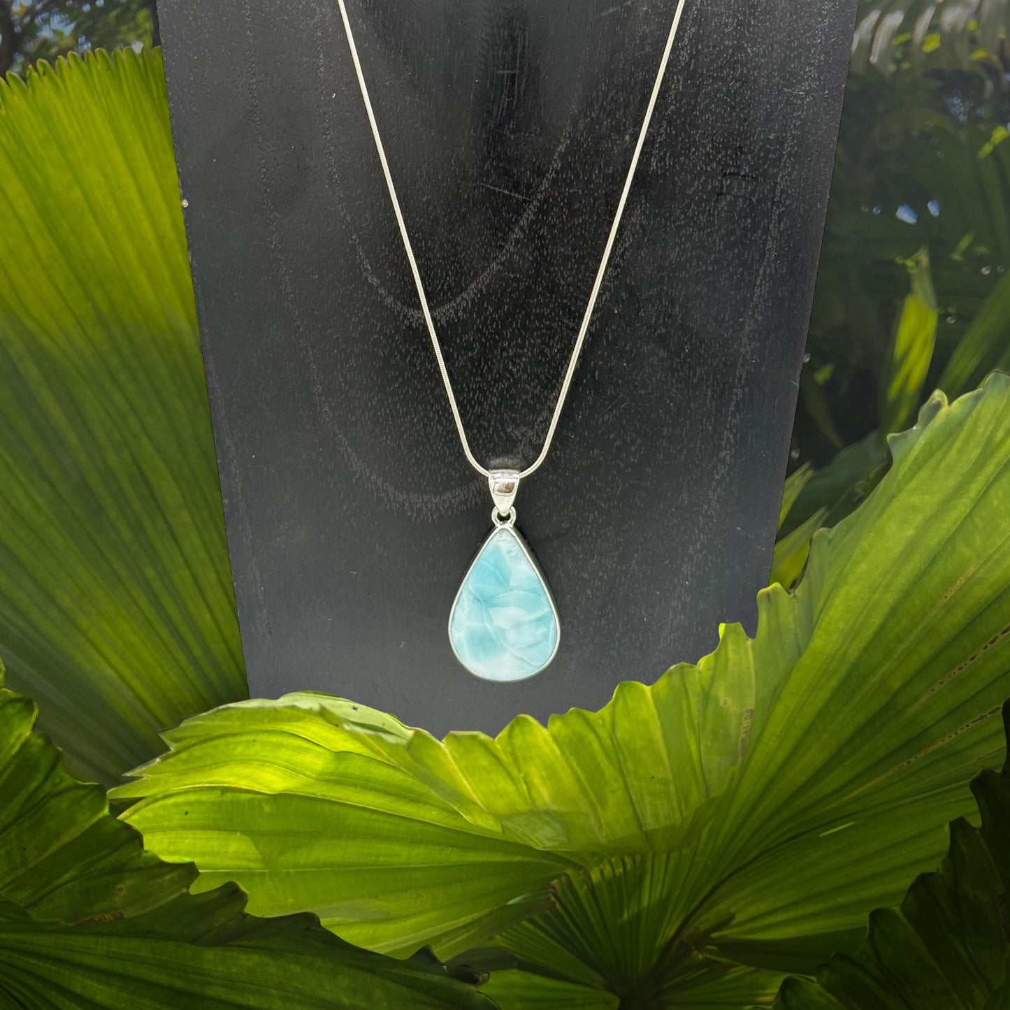 Larimar Anhänger auf eine Silber-kette umgeben von grünen Pflanzen
