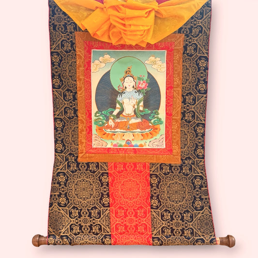 Weisse Tara Thangka mit dunkel-goldfarbener Stoffeinfassung, rotem Mittelband, gelbem Überwurf und Holzstab