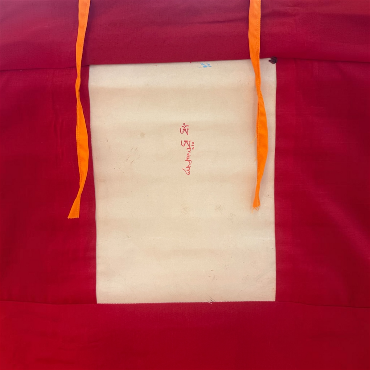 Rückseite des Weisse Tara Thangkas mit roter Stoffeinfassung, heller Bildrückseite, roter Schrift und gelben Bändern