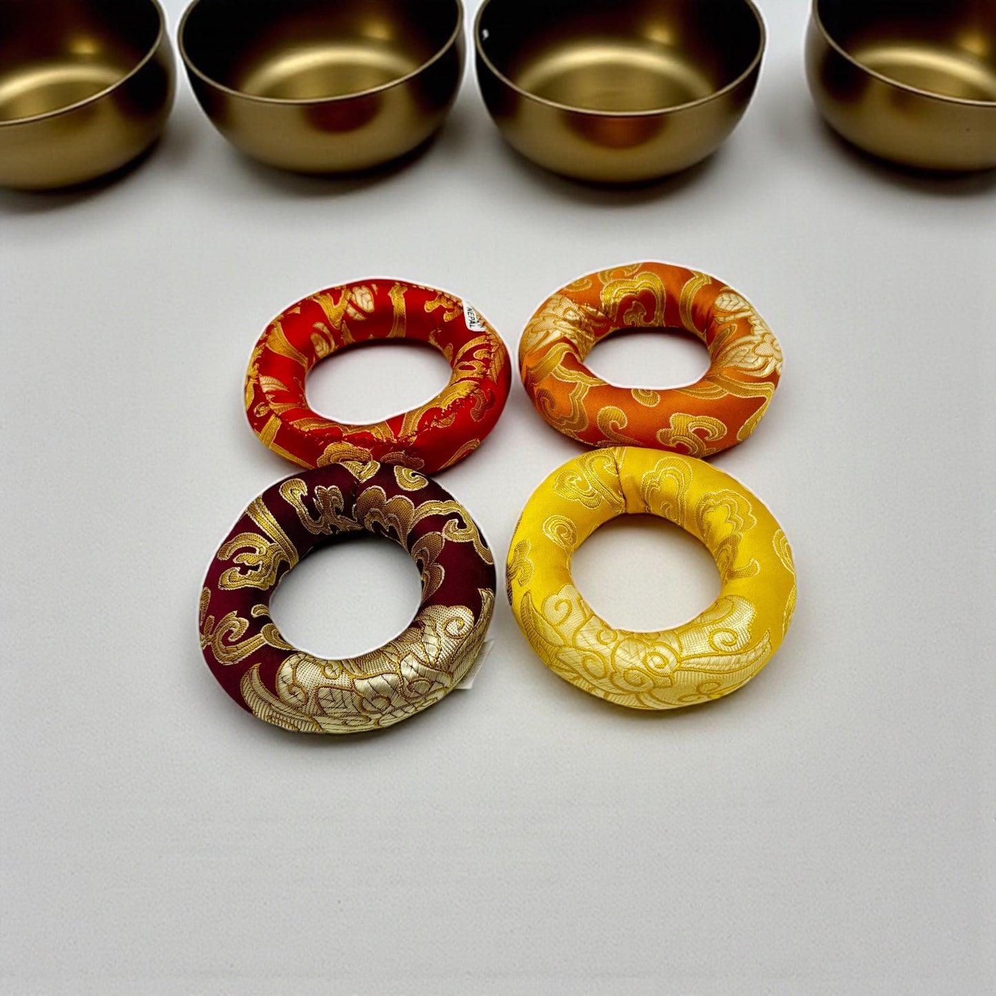 Kleine Klangschalenkissen in 4 verschiedenen Farben und Klangschalen in Hintergrund