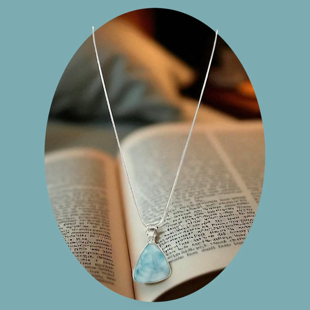 Zeigt Larimar Silber Anhänger mit einer Silber-Kette. ein offenes Buch im Hintergrund