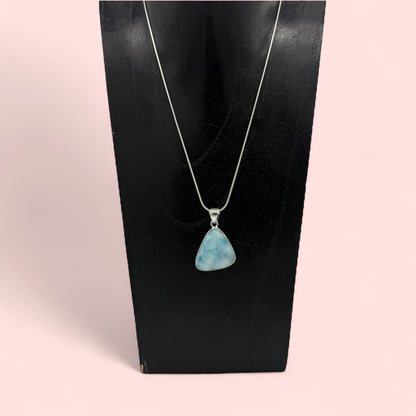 Zeigt Larimar Silber Anhänger mit einer Silber-Kette auf einen Schmuckständer. Rosa Hintergrund