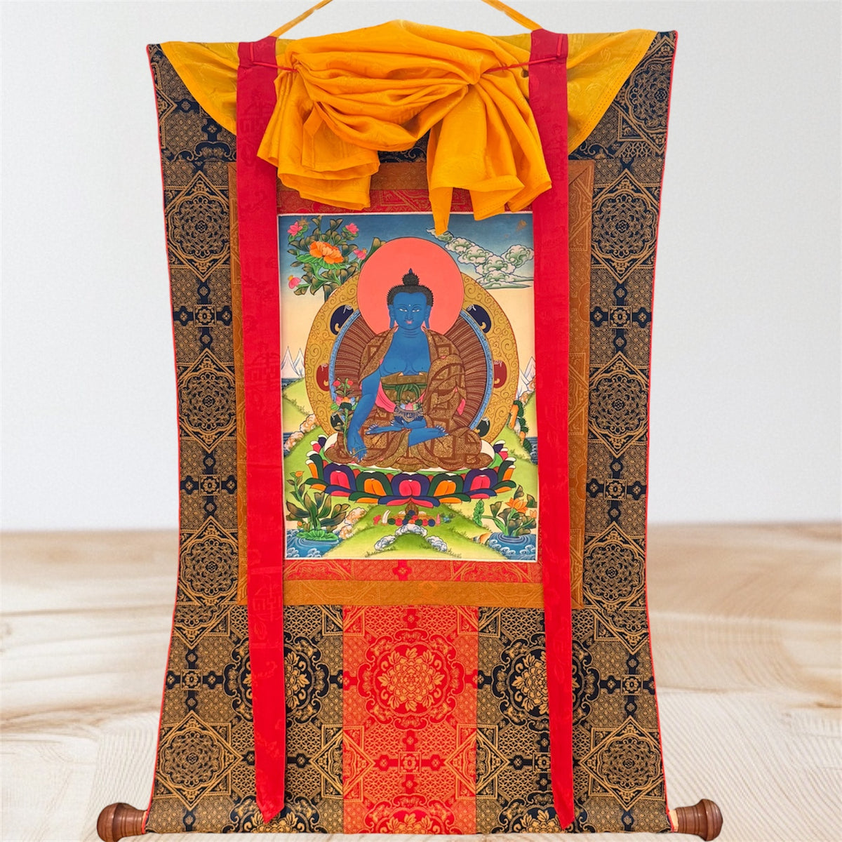 Medizin-Buddha Thangka in Blau mit gemusterter Stoffeinfassung, roten Bändern und gelbem Überwurf, Gesamtansicht