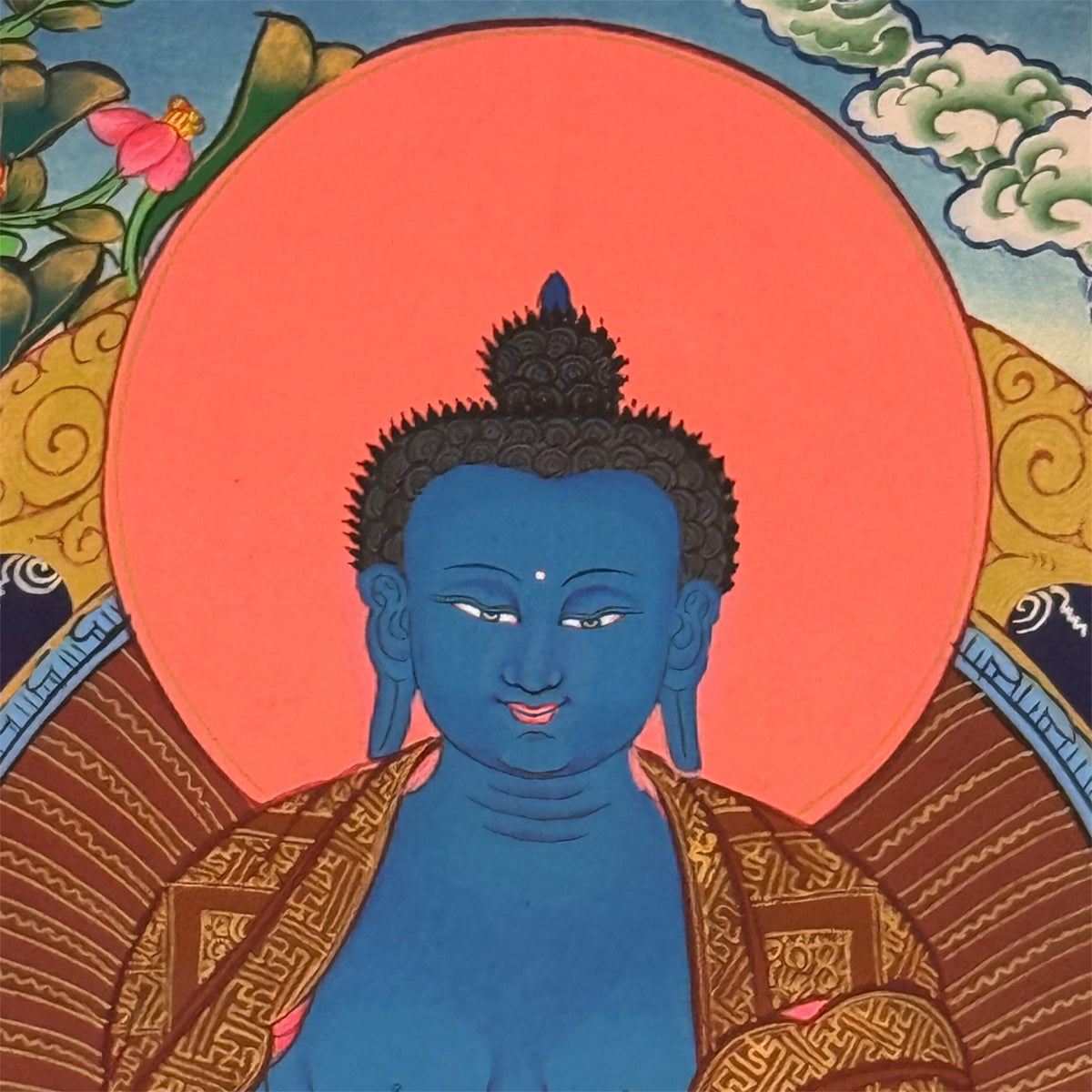 Detailansicht des blauen Medizin-Buddha mit fein gezeichnetem Gesicht, gemustertem Gewand und rot-orangefarbenem Heiligenschein