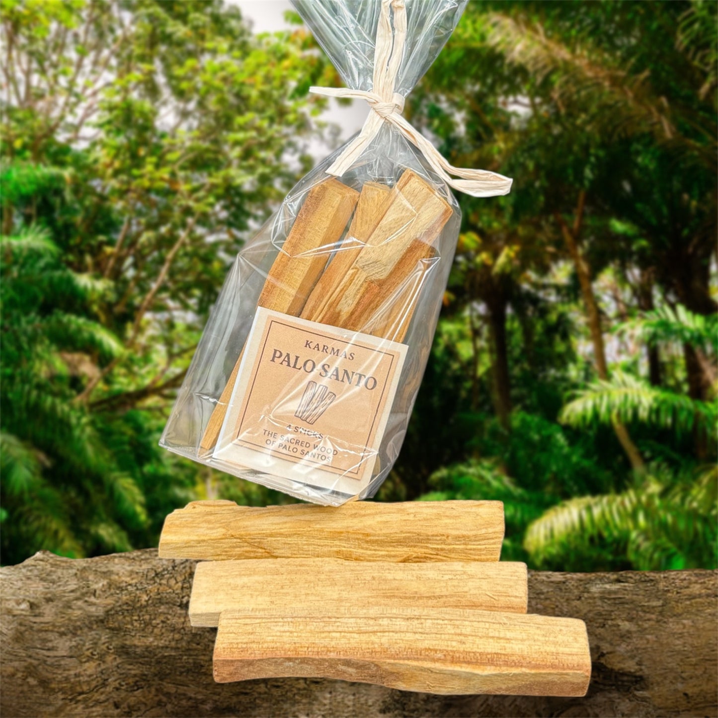 es zeigt 3 Holzstäben liegt offen und eine Plastik-Verpackung  vom Palo-Santo-Räucherstäbchen auf einem Baumstamm und im Hintergrund steht grüne Vegetation.