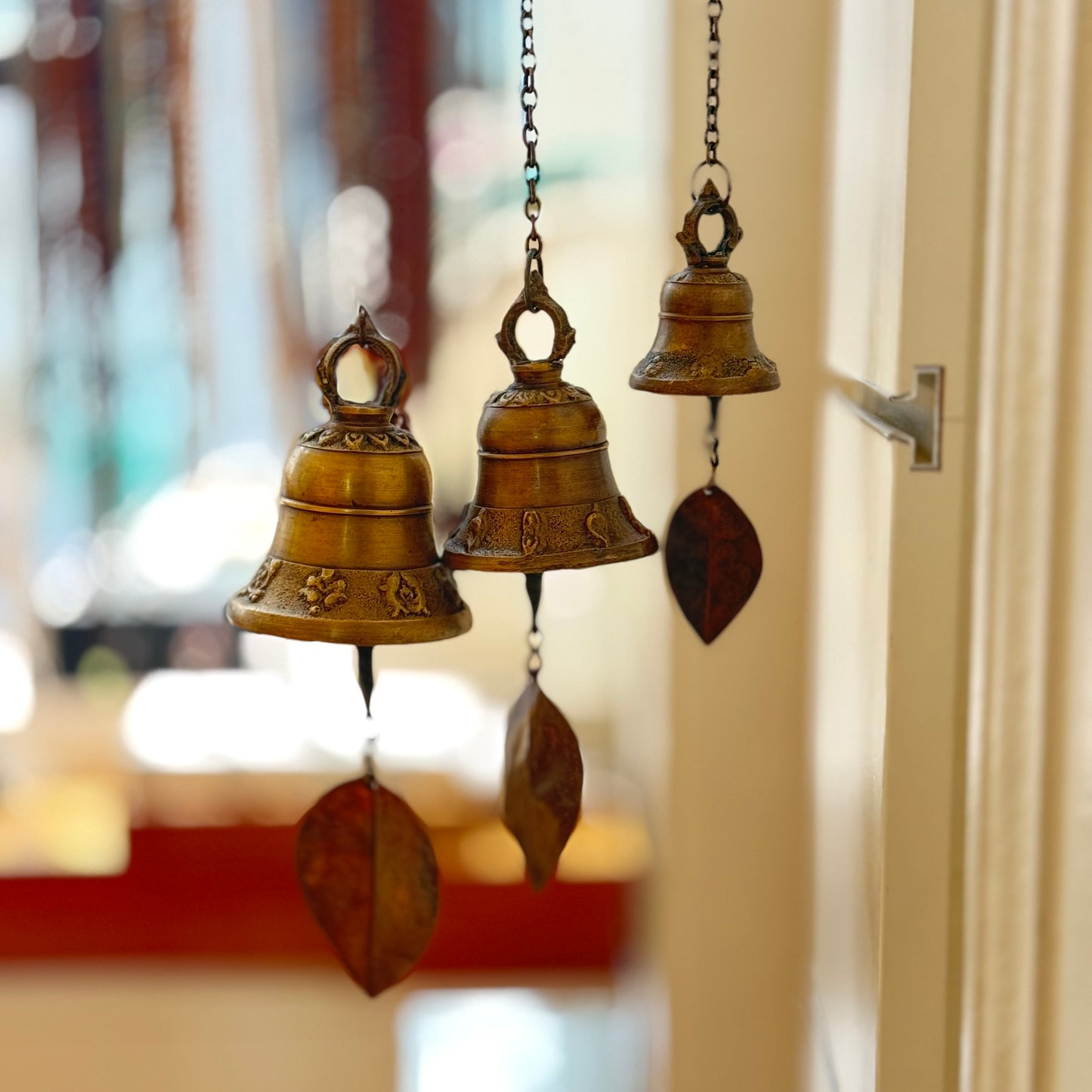 Windspiele in Glockenform aus Messing in drei Größen hängen in der Luft mit unscharfem Hintergrund